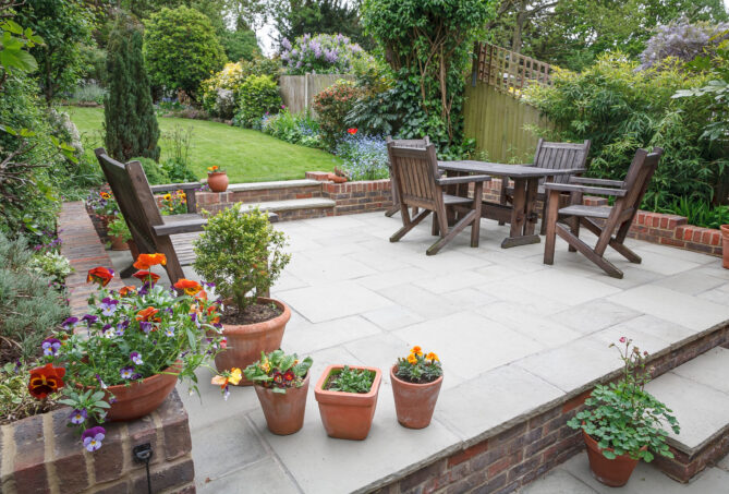 A porcelain slab garden patio pictured with a garden table and chairs and lots of plants and greenery.