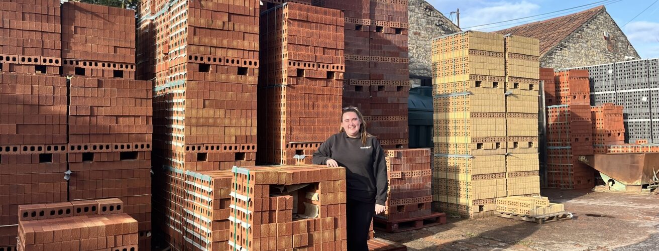 A woman standing among stacks of bricks at a builders merchants.