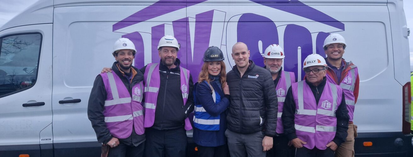 A man wearing a Brickability jacket stands with six members of the DIY SOS team in front of a DIY SOS van.