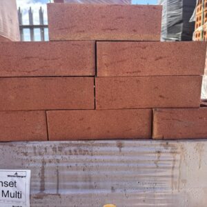 Eight red bricks stacked in a pyramid-like formation, sat among packs of red bricks.