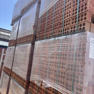 Several packs of red bricks that are half wrapped in plastic, neatly stacked in an outdoor yard.