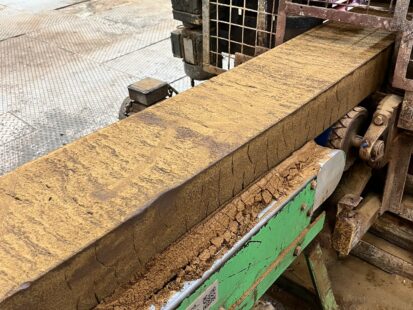 A long slab of clay extending from manufacturing equipment.