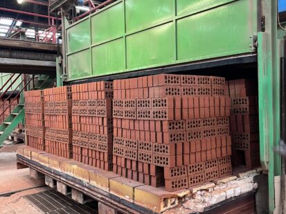 Three stacks of red bricks emerging from an industrial kiln in a warehouse.