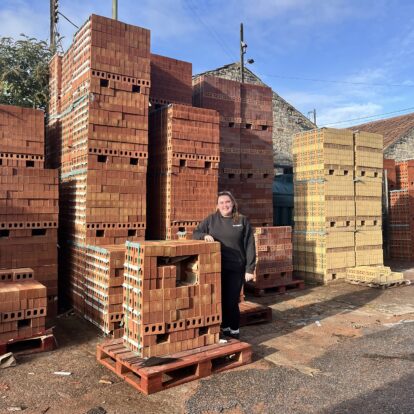 A woman standing among stacks of bricks at a builders merchants.