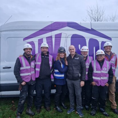 A man wearing a Brickability jacket stands with six members of the DIY SOS team in front of a DIY SOS van.