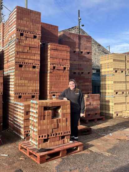 A woman standing among stacks of bricks at a builders merchants.