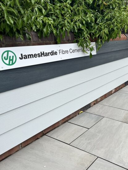 An image of Hardie Plank panels displayed on a low brick wall with porcelain paving on the ground in front.