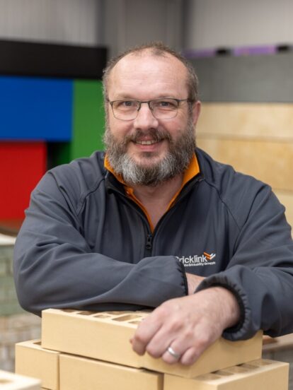 A man stands smiling leaning on a pile of bricks in a construction showroom.