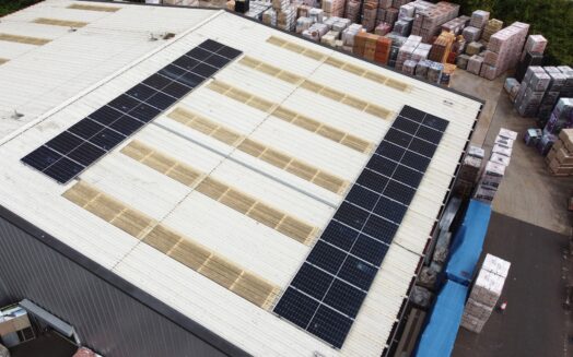 Two strips of solar panels on the roof of a warehouse with stacks of bricks in the background.