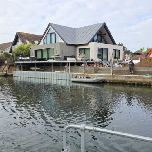 A modern house under construction and viewed from the water.