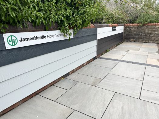 A short wall displaying panels of Hardie Plank Cladding with porcelain paving neatly laid on the ground in front.