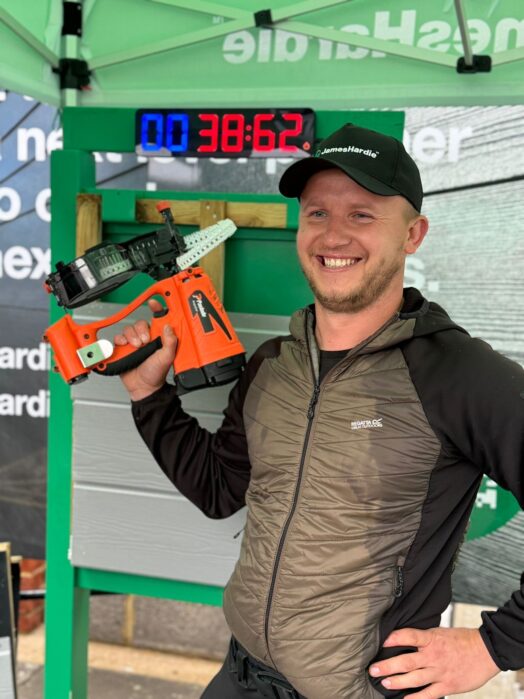 A man holding a nail gun stands in front of some wood-effect panels underneath a gazebo tent. A timer in the background reads 38.62 seconds.