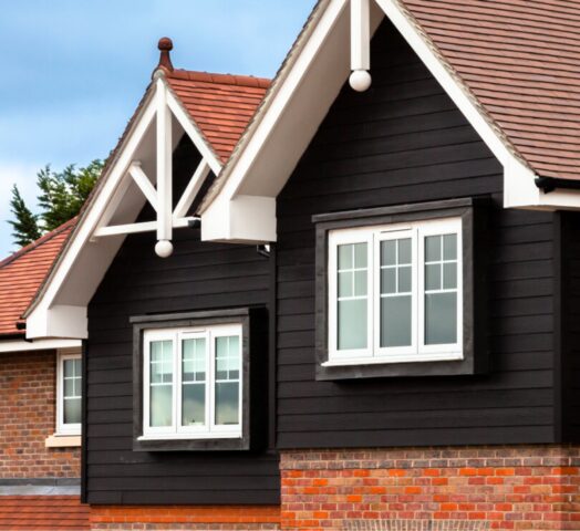 A photograph of the upper floor of two houses, featuring black weatherboard cladding and white timber details.