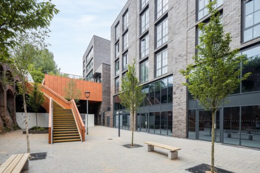 An image of a five storey, blue brick building next to an external orange staircase.