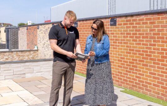 Two happy-looking people stood on a patio display looking at a brochure together.