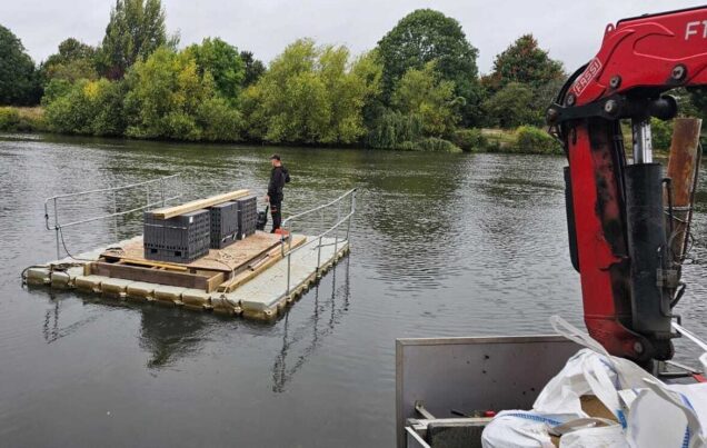A small barge on a river carrying three stacks of dark blue bricks.