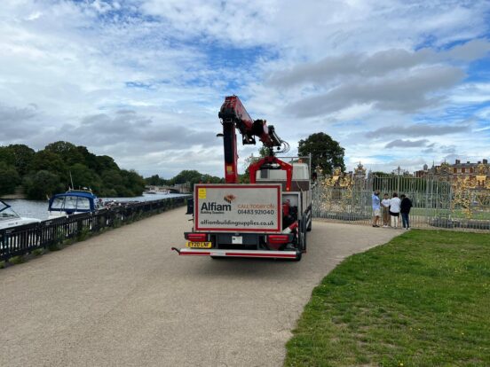 An Alfiam truck sits in between a river and the golden gates of Hampton Court, with the palace visible in the background.