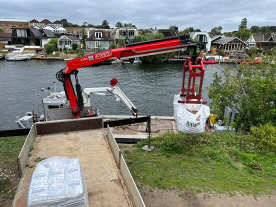 A crane lifts Alfiam aggregate bags onto a barge in a river.
