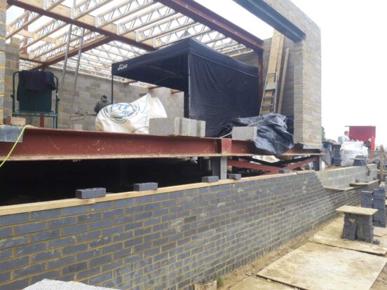 A view of a home under construction with a half-built dark blue brick wall and stacks of blue bricks nearby.