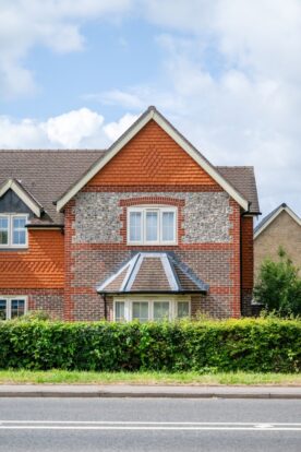 A brick and flint block house partially obscured by a hedge.