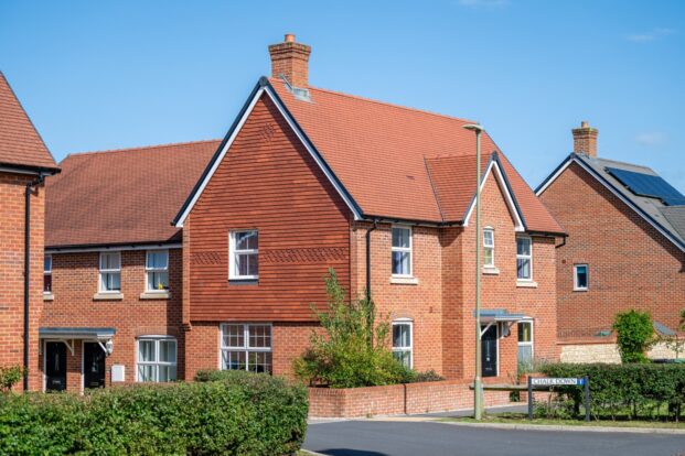 Red-brick house in a new housing estate under a blue sky.