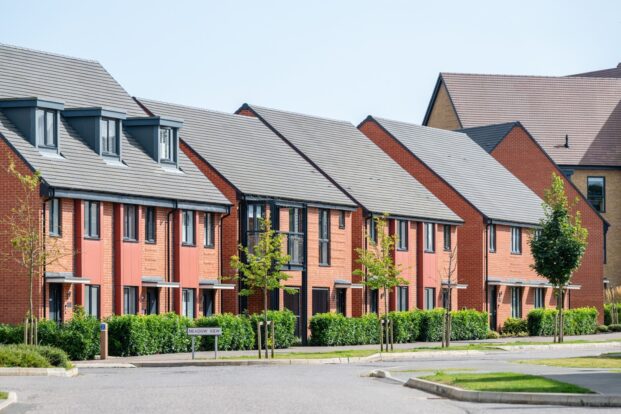 A row of red-brick homes with dark roofing and red cladding.