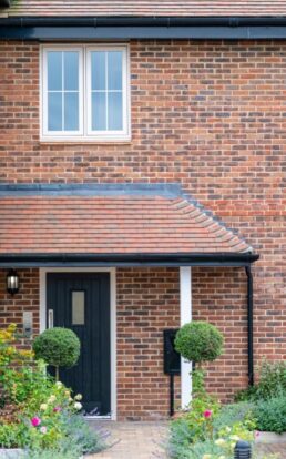 The front door and first floor window of a red-brick home.