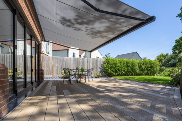A photo of a garden deck with an awning on a sunny day, with houses in the background visible over the garden hedge.