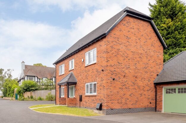 Red-brick detached house with old fashioned English house in the background.