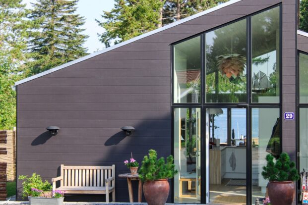 A modern house in anthracite grey wood-effect panels. A forested area is visible in the background.
