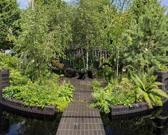 A garden installation encircled by a dark grey brick wall with a brickwork bridge and ground.
