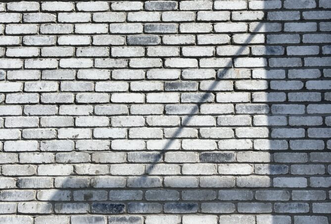 A grey wall build from concrete bricks, with shadows falling across the surface.