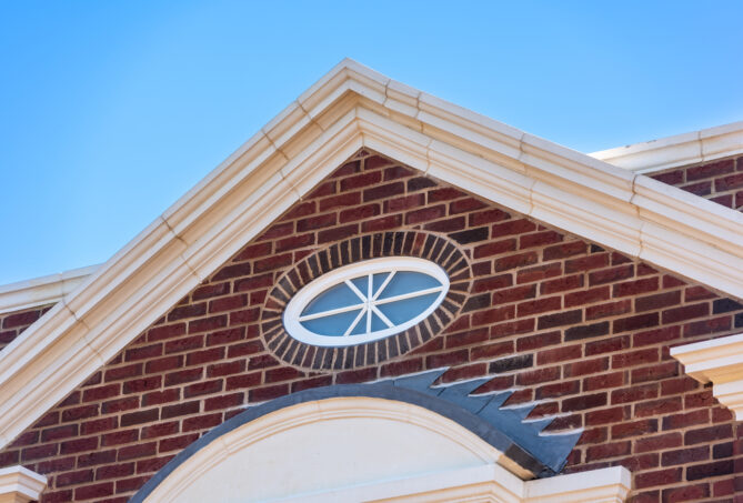 A gable front of a red brick building featuring a round window.