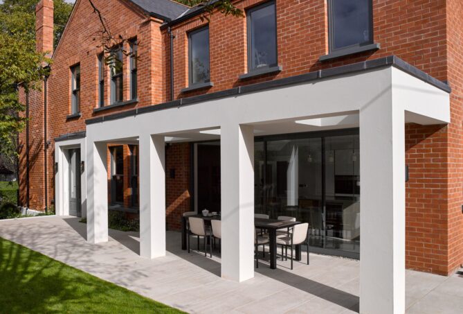 A red brick house with a large stone pergola projecting from the rear into the garden.