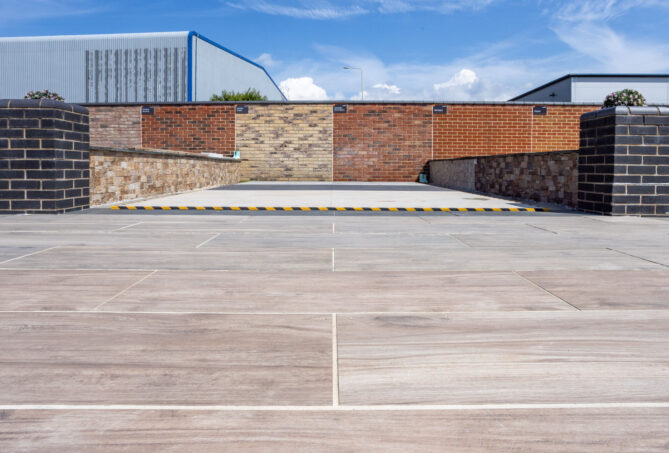 A large porcelain paving display with a brick wall running along the back. Set against a blue sky with wispy clouds.