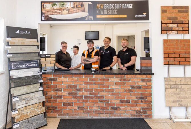 Five people stood behind the counter at a builders merchants. The counter is surrounded by brick samples and displays.