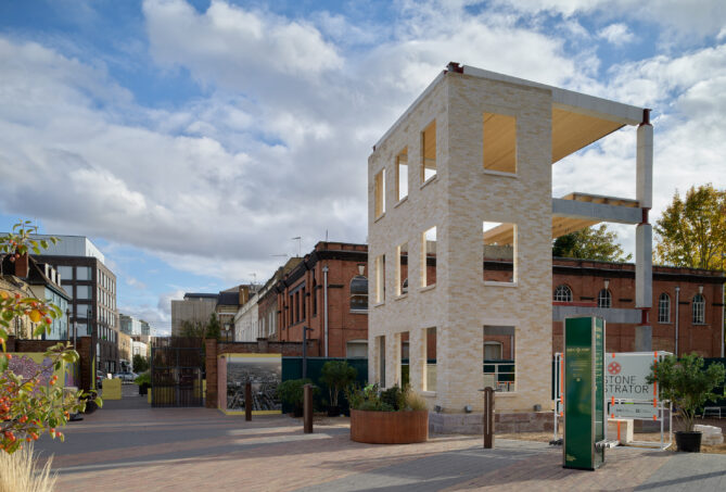 Front view of stone demonstrator project at earls court featuring stone bricks on facade. surrounded by pavement, greenery and london buildings.