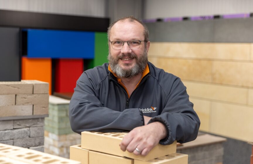 A man stands smiling leaning on a pile of bricks in a construction showroom.
